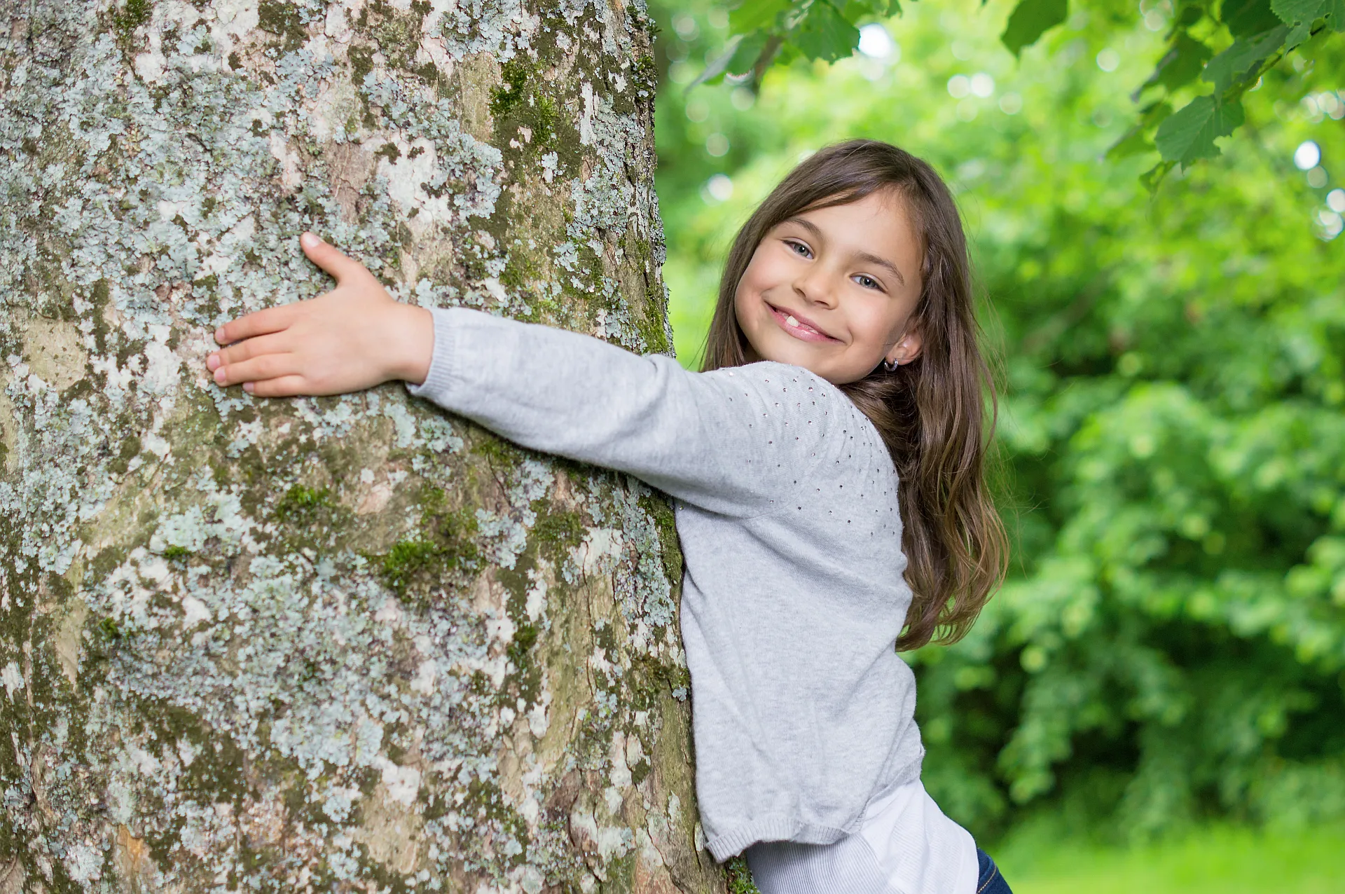 Maedchen umarmt laechelnd einen Baum