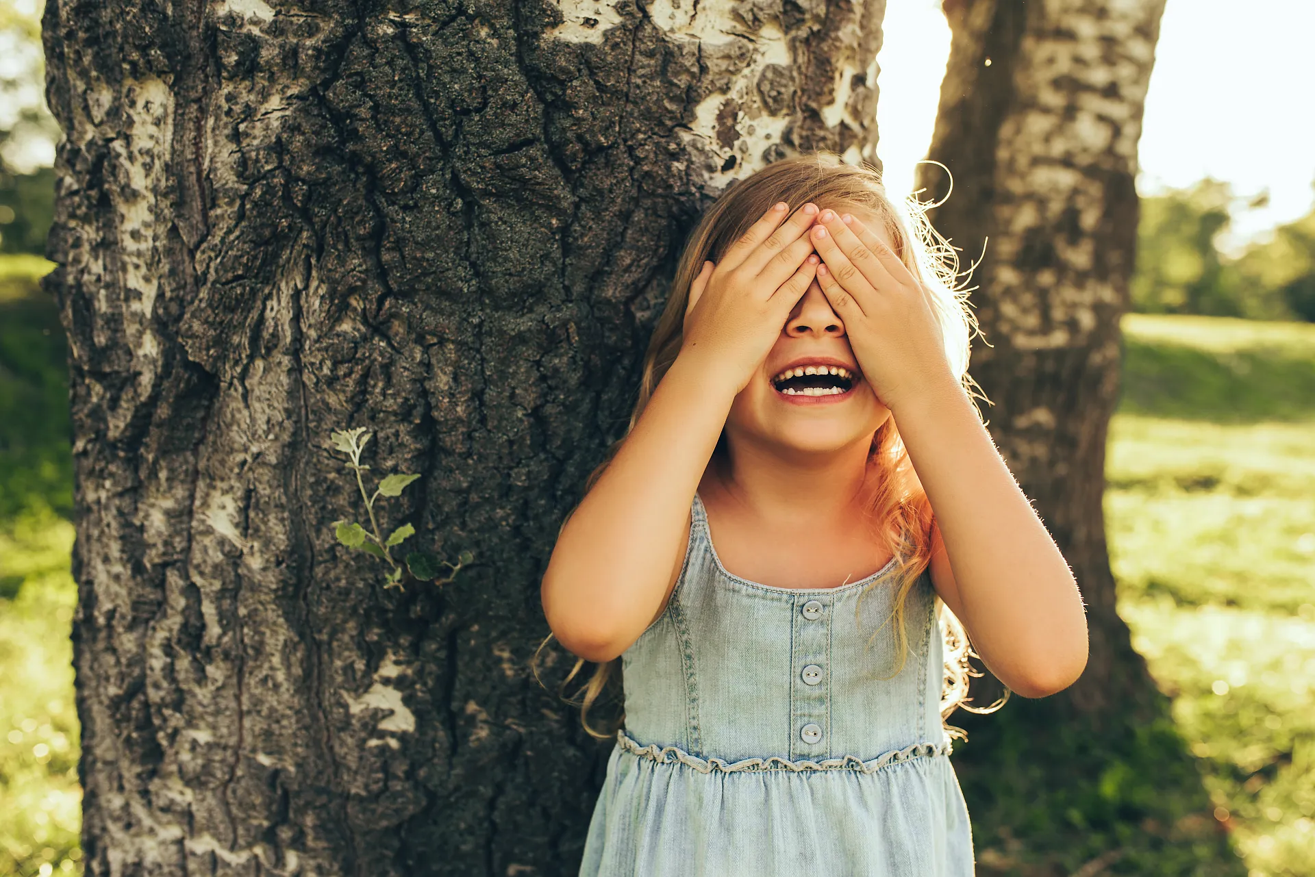 Maedchen spielt lachend Verstecken am Baum